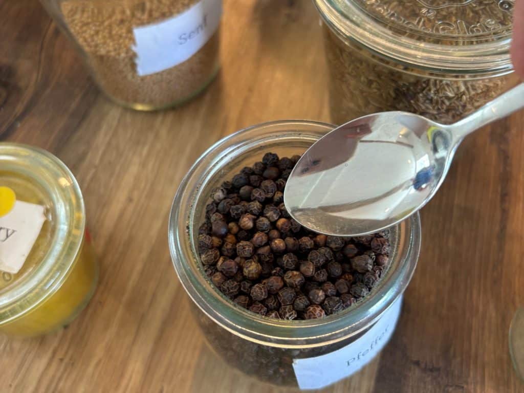 In den Salzwelten Bad Sassendorf wird ein silberner Löffel über ein Glas mit schwarzen Pfefferkörnern gehalten, das von weiteren Gewürzgläsern auf einem Holztisch umgeben ist.
