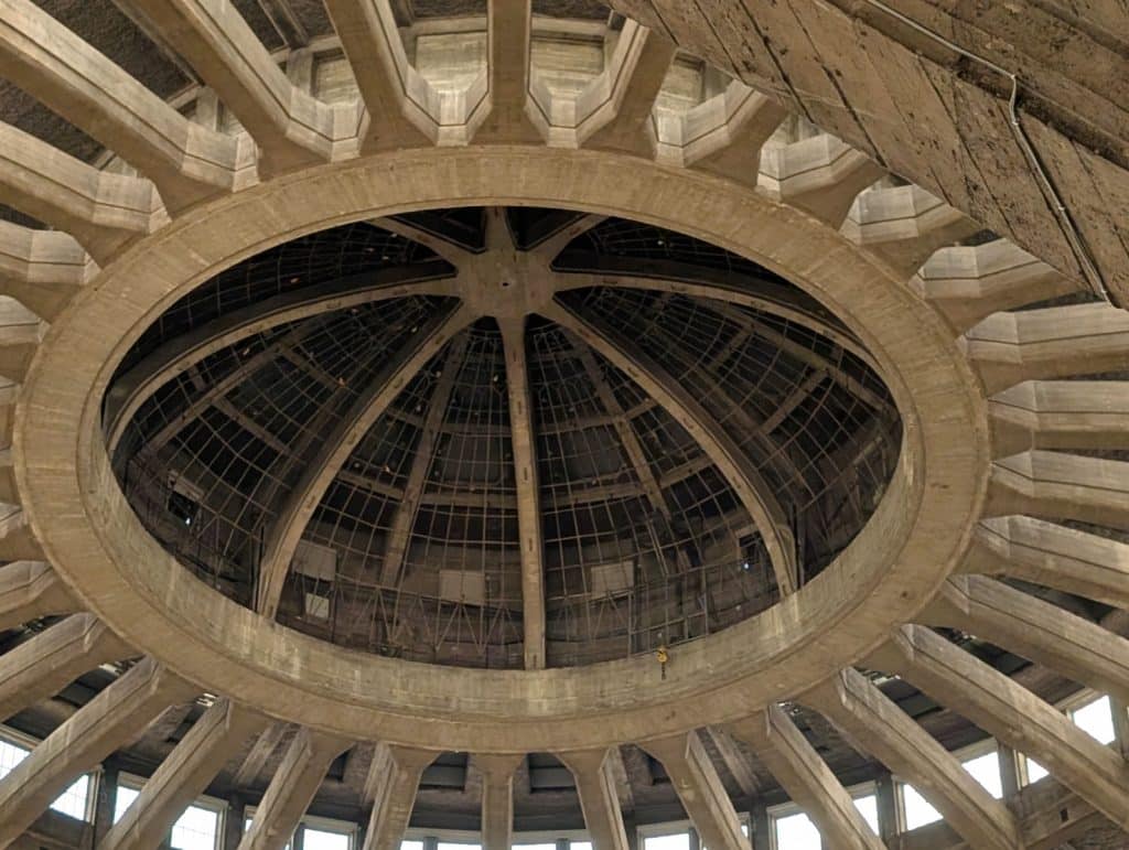 Blick nach oben in die monumentale, gestufte Betonkuppel der Jahrhunderthalle in Breslau, deren zentrale Öffnung durch eine filigrane Stahl-Glas-Konstruktion abgeschlossen wird.