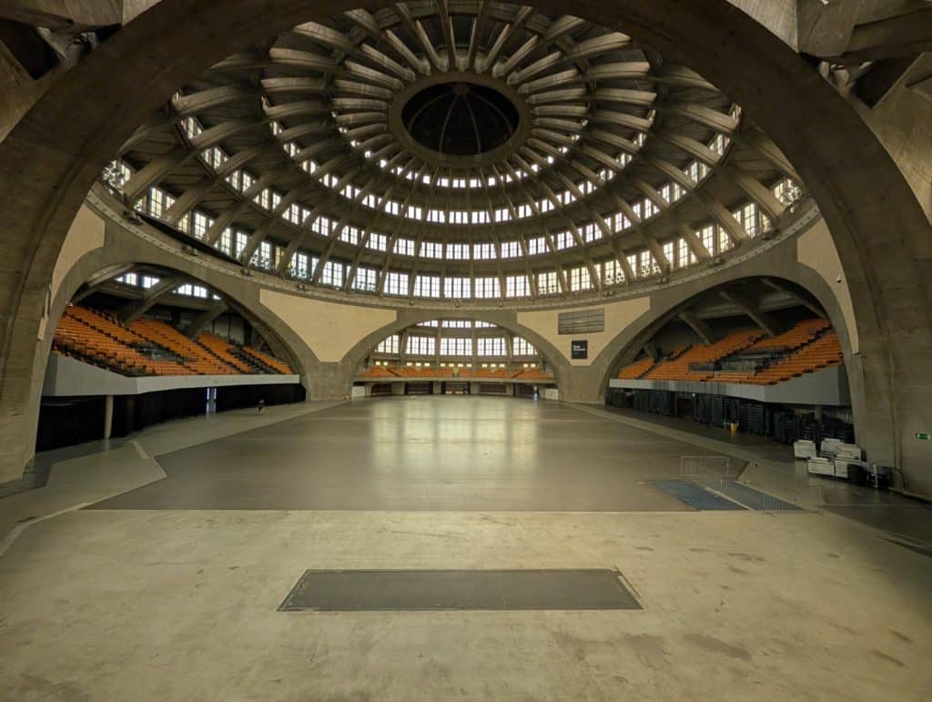 Innenansicht der Breslauer Jahrhunderthalle mit ihrer monumentalen, gerippten Betonkuppel, die über einer weitläufigen, leeren Veranstaltungsfläche und ansteigenden Sitzreihen thront.