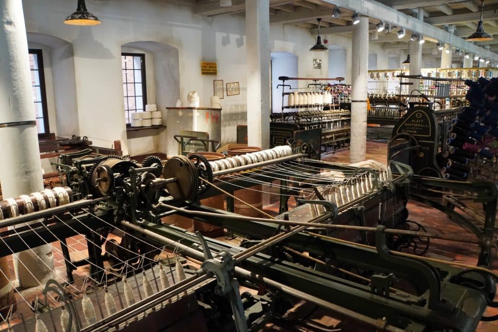 Historische Spinnmaschinen und Webstühle mit zahlreichen Garnspulen füllen eine Ausstellungshalle in der Weiße Fabrik Łódź.