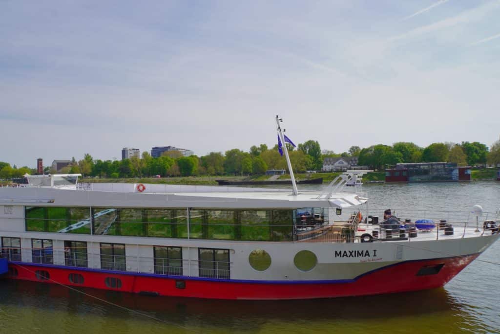 Das Flusskreuzfahrtschiff MS Maxima liegt am Anleger in Bratislava auf der Donau, erkennbar an seinem weißen Rumpf mit roter Unterseite und der Aufschrift „MAXIMA I“.