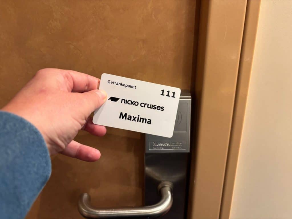 Eine Hand hält eine weiße Schlüsselkarte mit der Aufschrift „nicko cruises Maxima“ vor das elektronische Türschloss der Kabine 111 auf dem Flusskreuzfahrtschiff Nicko Donau Maxima.