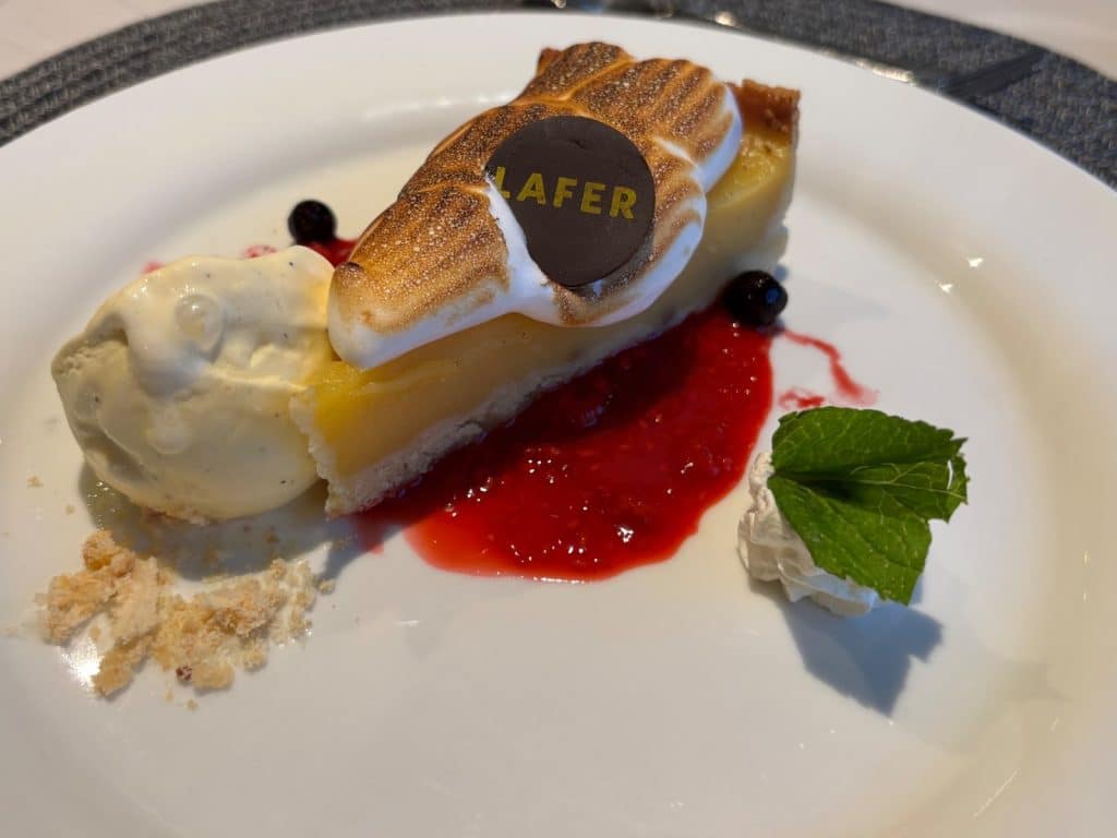 Ein Stück Zitronen-Baiser-Tarte nach einem Rezept von Johann Lafer, serviert auf der Maxima mit Vanilleeis, Himbeersauce, Crumble und einem Minzblatt.