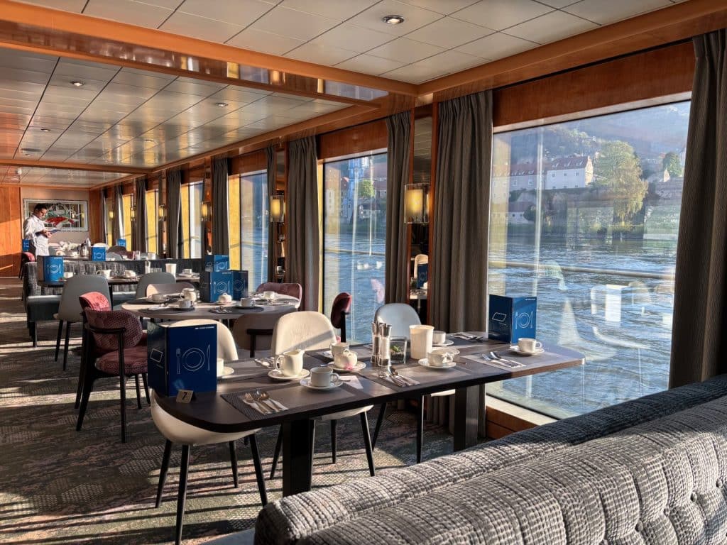 Das Restaurant der Maxima von nicko cruises auf der Donau ist hell und modern mit eingedeckten Frühstückstischen vor großen Panoramafenstern gestaltet, die einen Blick auf das vorbeiziehende Ufer bieten.