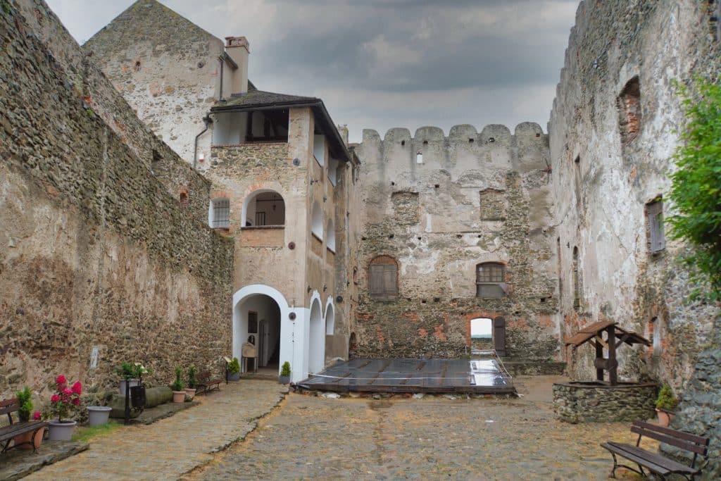 Der gepflasterte Innenhof der Bolkoburg in Niederschlesien zeigt historische Steinmauern mit Rundbögen, einen alten Brunnen und Holzbänke unter einem bewölkten Himmel.