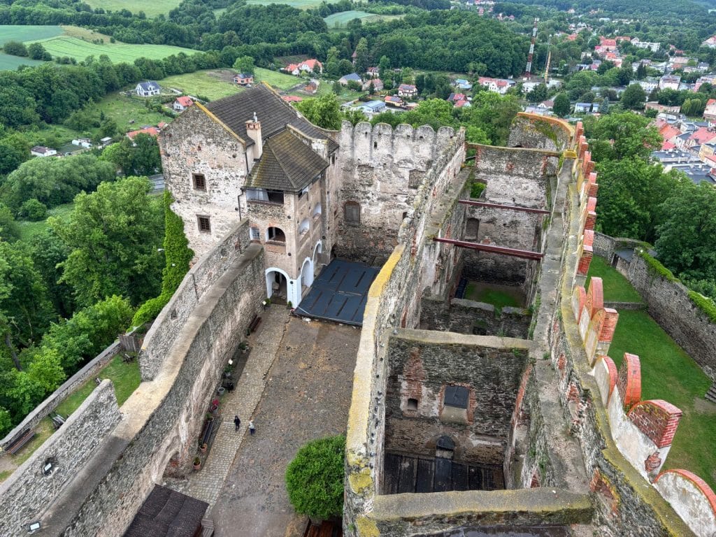 Blick von oben in den Innenhof der Bolkoburg-Ruine in Niederschlesien mit ihren massiven Steinmauern, einem erhaltenen Wohngebäude und den umliegenden grünen Hügeln und Wäldern.