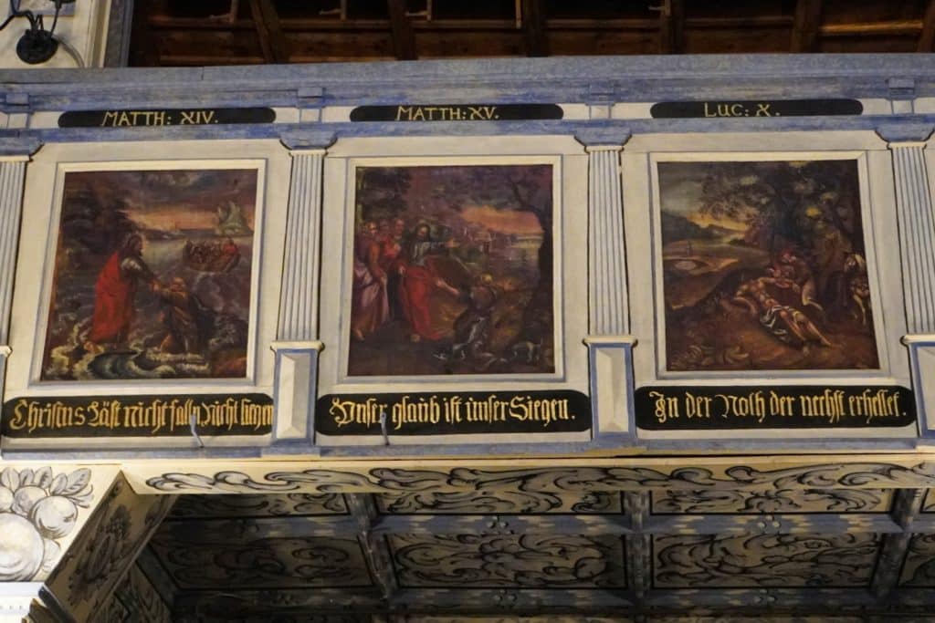 Drei bemalte Brüstungsfelder der Friedenskirche in Jawor, Niederschlesien, zeigen biblische Szenen mit lateinischen Kapitelangaben und deutschen Inschriften, getrennt durch dekorative Säulenelemente.