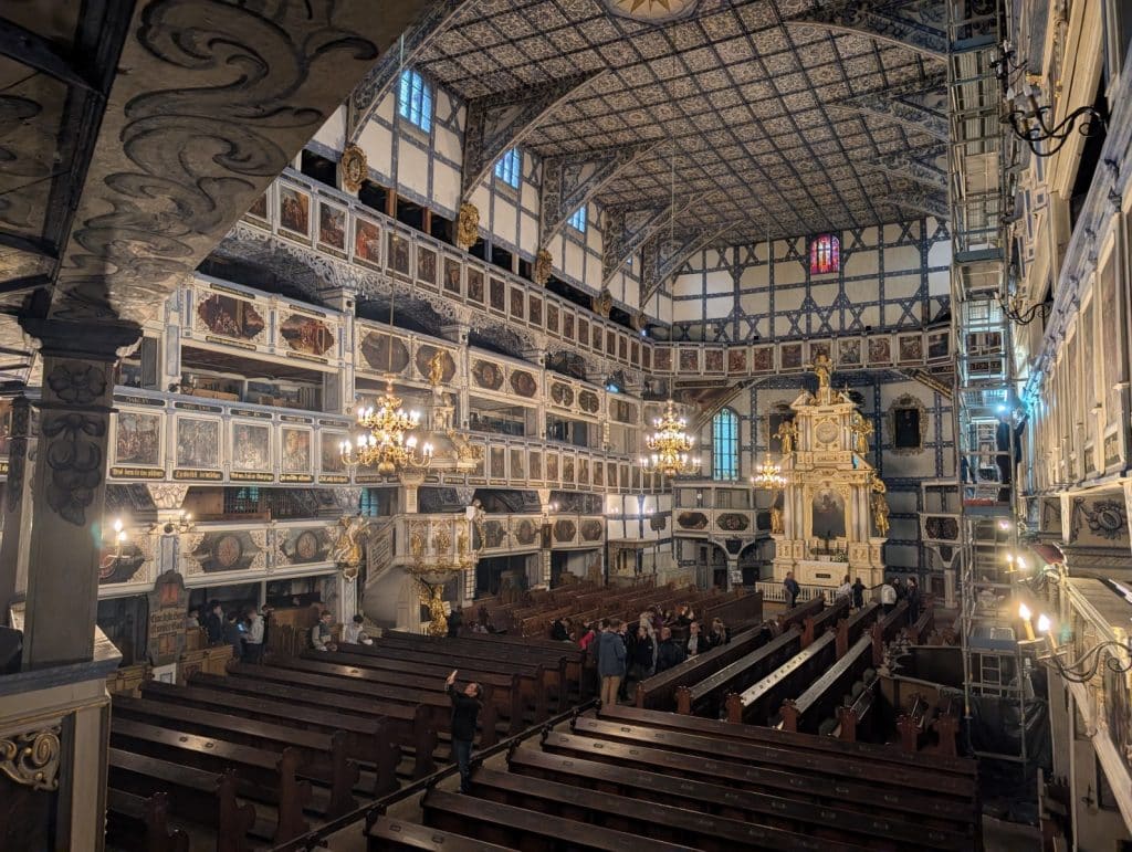 Der prunkvolle Innenraum der Friedenskirche in Jawor, Niederschlesien, zeigt mehrstöckige, reich bemalte Holzemporen, eine kunstvolle Kassettendecke und einen goldenen Altar vor den hölzernen Kirchenbänken.