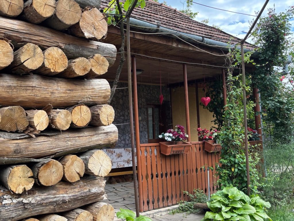 Eine rustikale Terrasse in der Region Timis, geschmückt mit Blumenkästen und roten Herzanhängern, neben der ein hoher Stapel ordentlich geschichteter Baumstämme lagert.