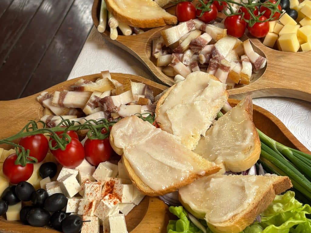 Zwei hölzerne Servierplatten präsentieren eine traditionelle Vorspeise im Complexul Turistic Valea lui Liman, bestehend aus mit Speck bestrichenem Brot, Speckwürfeln, Käsevariationen, Kirschtomaten, Oliven und Frühlingszwiebeln.