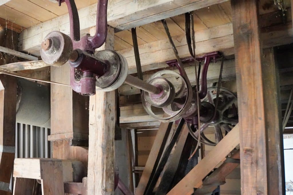 Historische Transmissionswellen und Riemenscheiben aus Metall und Holz im Inneren einer alten Mühle in der Region Timiș.
