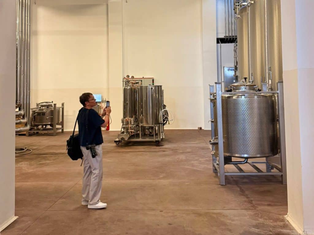 Eine Person fotografiert bei einem Weingut-Rundgang in der Region Timiș die großen Edelstahltanks und Abfüllanlagen in einer hellen Produktionshalle.