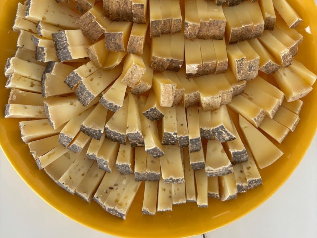 Eine gelbe Platte, die dicht mit fächerförmig angeordneten Käsescheiben einer Käseplatte aus einem Weingut in der Region Timis belegt ist, wobei die dunkle Rinde der Käsestücke nach außen zeigt.