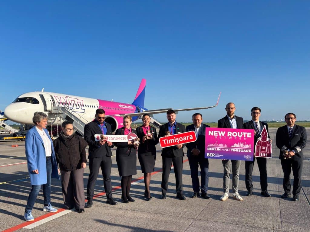 Eine Gruppe von offiziellen Vertretern und Flugpersonal steht vor einem Wizz-Air-Flugzeug auf dem Rollfeld, um mit Schildern den offiziellen Beginn der neuen Flugverbindung zwischen Berlin und Timișoara in Rumänien zu feiern.