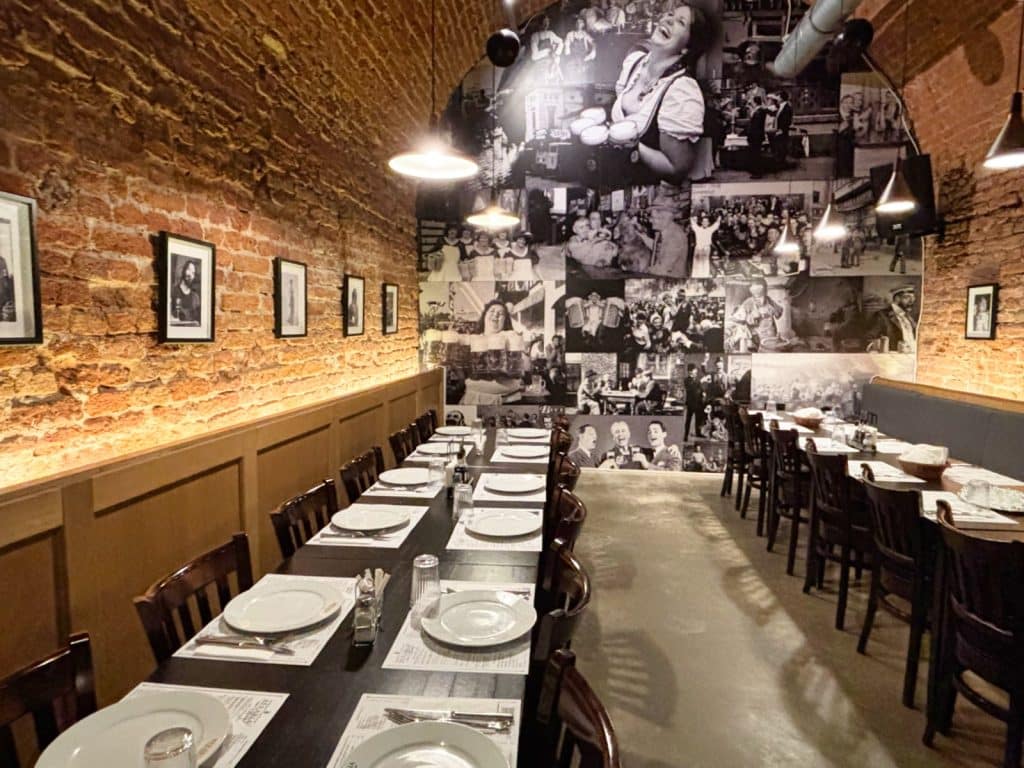 Innenansicht eines Restaurants in der Brauerei Timișoara mit langen, eingedeckten Holztischen vor einer rustikalen Ziegelwand und einer großen Fotocollage mit historischen Motiven an der Stirnseite.