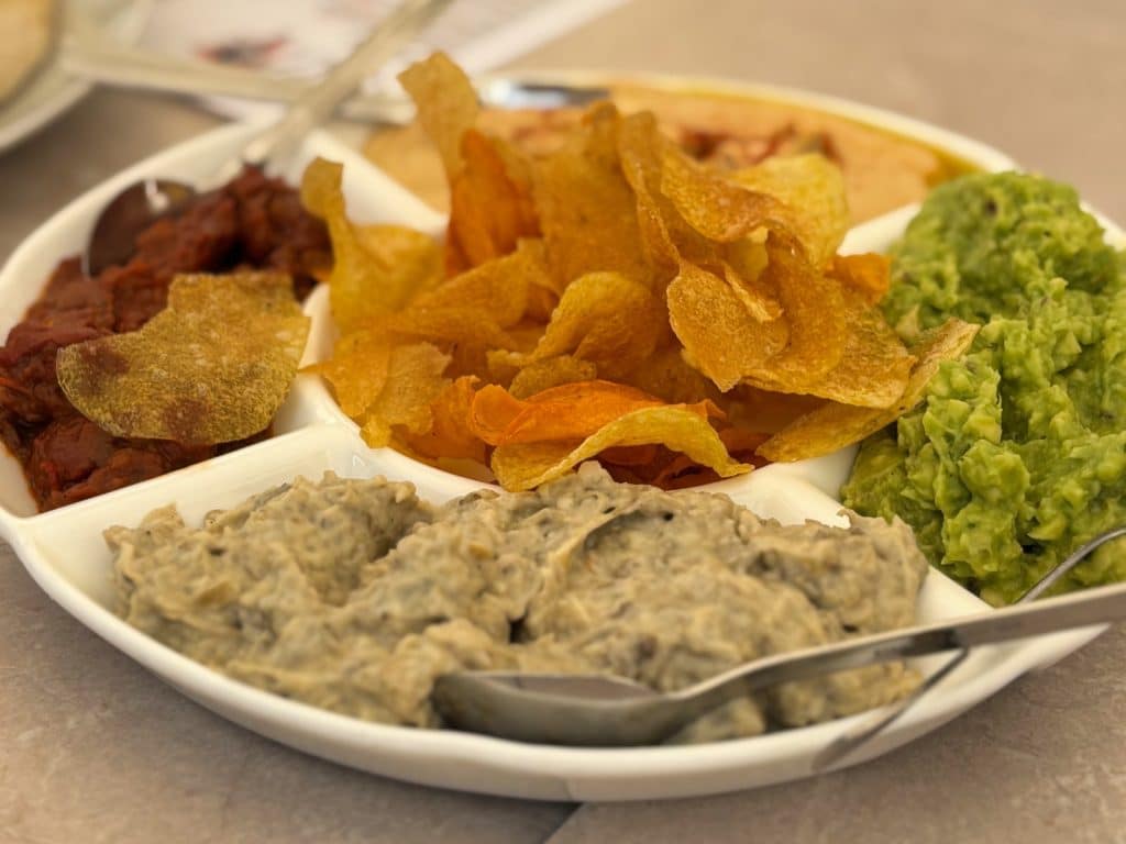 Ein Vorspeisenteller im Restaurant Pepper in Timișoara mit verschiedenen Dips wie Guacamole, Hummus und Auberginencreme, in dessen Mitte knusprige Kartoffelchips angerichtet sind.