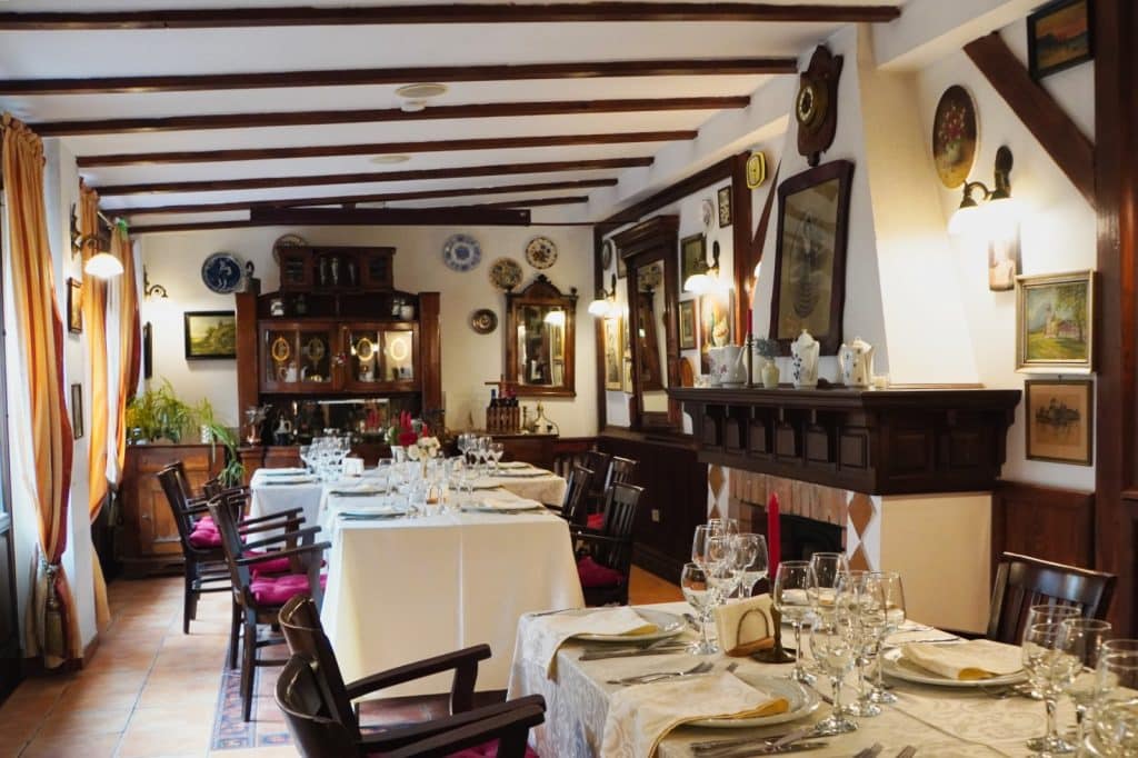Der Innenraum des Restaurants Casa del Sole in Timișoara ist rustikal mit dunklen Deckenbalken, einem Kamin und weiß gedeckten Tischen mit Weingläsern gestaltet. Die Wände sind mit zahlreichen gerahmten Bildern, dekorativen Tellern und antiken Holzmöbeln geschmückt, was eine gemütliche Atmosphäre schafft.