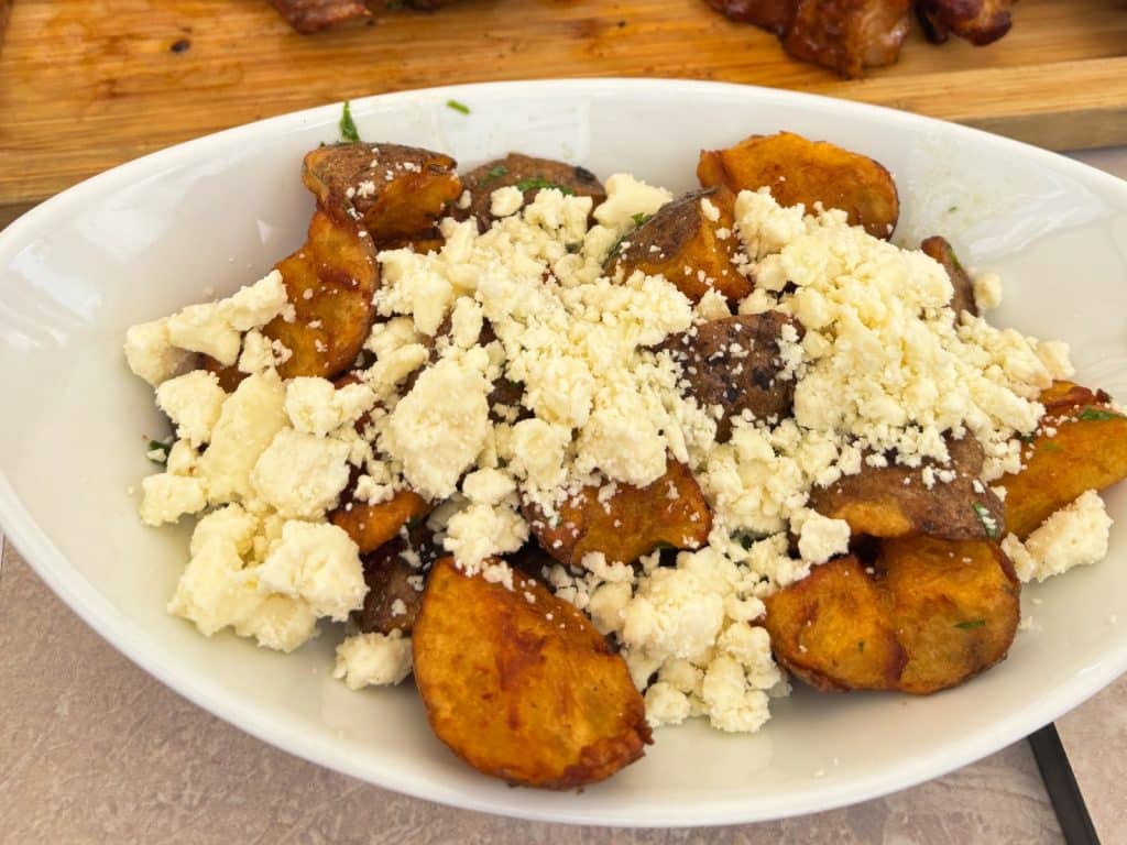 Eine weiße Schale mit goldbraun gerösteten Pepper-Kartoffeln, die großzügig mit zerbröckeltem weißem Schafskäse bestreut sind, serviert in einem Restaurant in Timișoara.