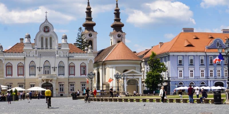 Der weitläufige, gepflasterte Vereinigungsplatz in Timișoara mit der markanten serbisch-orthodoxen Kathedrale und ihren zwei Zwiebeltürmen im Hintergrund, umgeben von historischen, farbenfrohen Gebäuden unter leicht bewölktem Himmel.