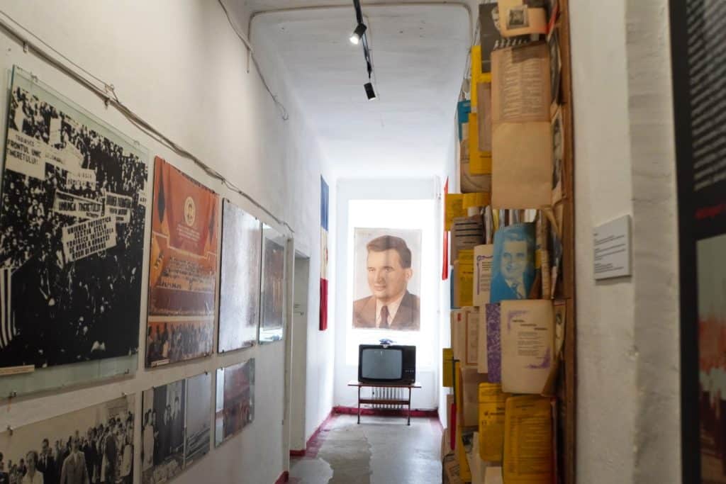 Ein schmaler Gang im Museum in Timișoara ist mit historischen Plakaten, Dokumenten und Fotos aus der kommunistischen Ära gesäumt, während am Ende des Flurs ein Porträt von Nicolae Ceaușescu über einem alten Röhrenfernseher hängt.