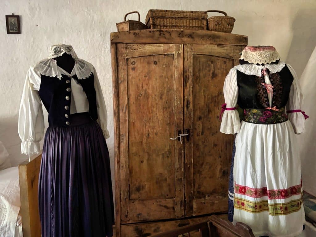 Zwei traditionelle rumänische Trachten auf Schaufensterpuppen stehen neben einem rustikalen Holzschrank im Museumsdorf in Timișoara.