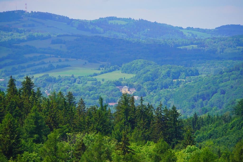 Blick über die bewaldeten Hügelketten der niederschlesischen Seite des Riesengebirges auf ein historisches Gebäude mit markanter Kuppel im Tal.