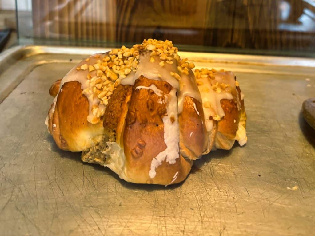 Ein frisch gebackenes Posener Martinshörnchen mit weißer Glasur und gehackten Nüssen liegt auf einem metallischen Backblech in einer Auslage.