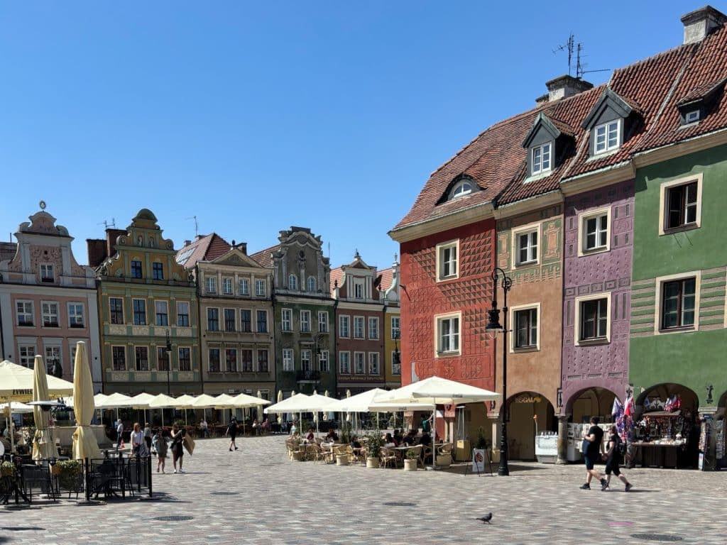 Blick auf den historischen Marktplatz in Posen mit seinen charakteristischen, bunt bemalten Giebelhäusern und belebten Straßencafés unter weißen Sonnenschirmen bei strahlendem Sonnenschein.