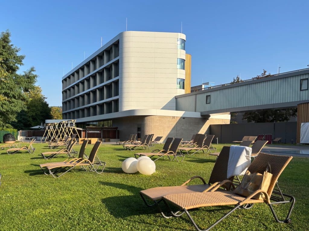 Sonniger Garten der Emser Therme in Bad Ems mit zahlreichen Liegestühlen auf einer grünen Rasenfläche vor der modernen Fassade des ThermenHotels.