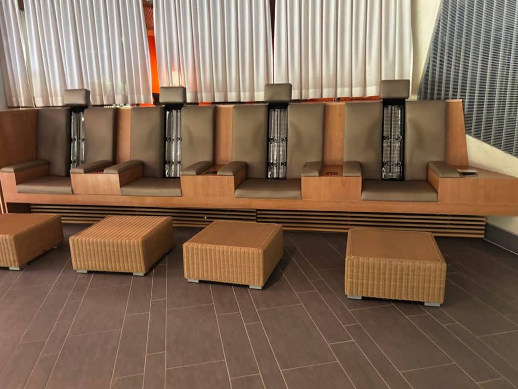 Vier Infrarotsitze in der Emser Therme mit braunen Polstern, hölzernen Armlehnen und davor platzierten, quadratischen Hockern aus Korbgeflecht.