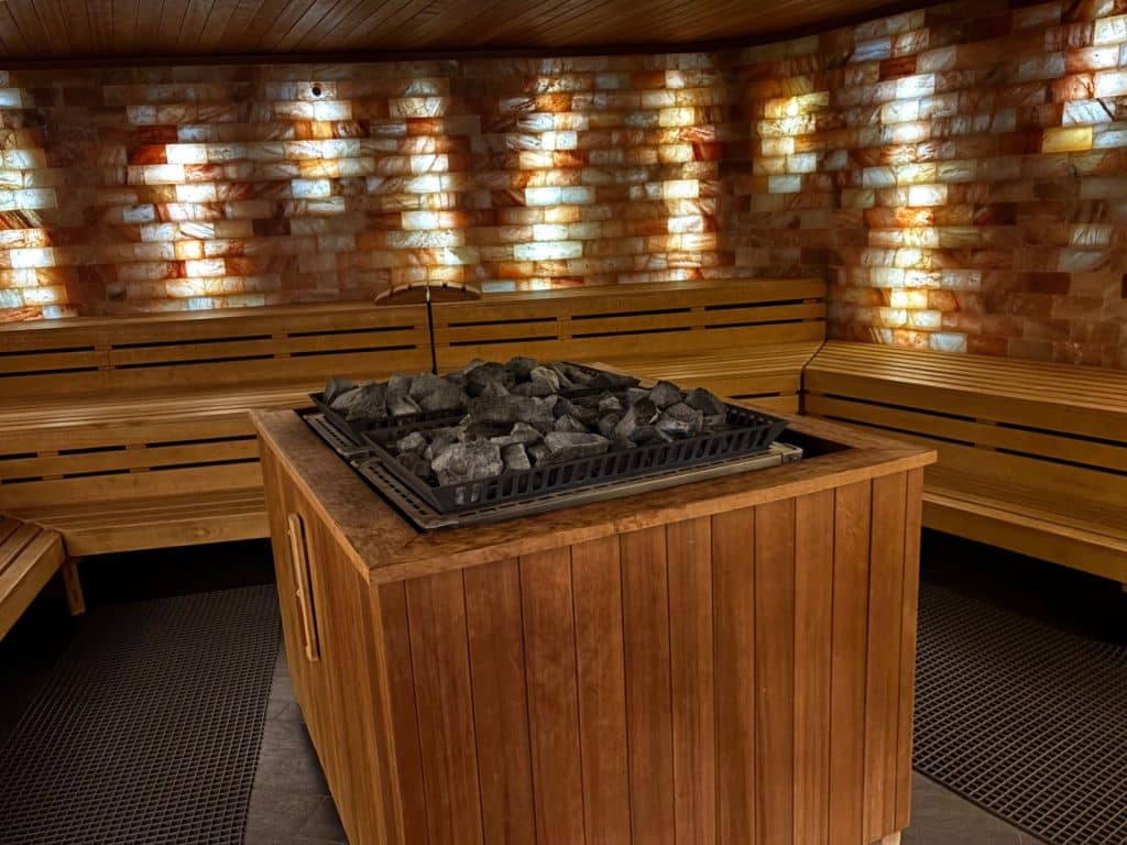 Innenansicht der Salzsauna in der Emser Therme mit beleuchteten Wänden aus Salzsteinen, hölzernen Sitzbänken und einem zentralen Saunaofen mit dunklen Steinen.