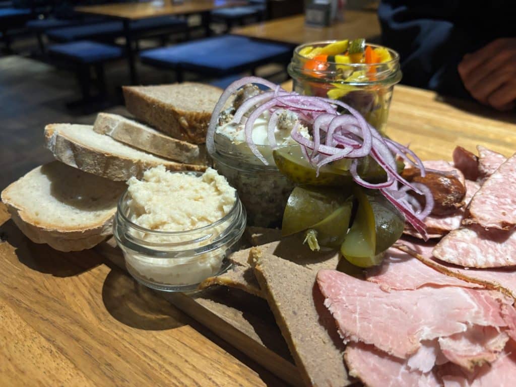 Eine rustikale Brotzeitplatte im Restaurant Targowa in Breslau mit verschiedenen Fleischsorten, Schmalz, Meerrettich, Gewürzgurken, roten Zwiebelringen und mehreren Scheiben frischem Brot auf einem Holzbrett.