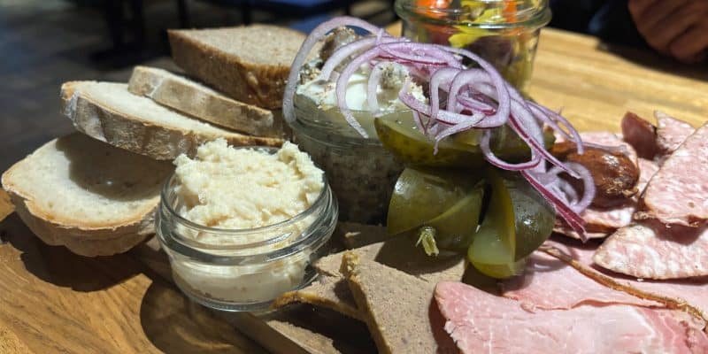 Eine rustikale Brotzeitplatte im Restaurant Targowa in Breslau mit verschiedenen Fleischsorten, Schmalz, Meerrettich, Gewürzgurken, roten Zwiebelringen und mehreren Scheiben frischem Brot auf einem Holzbrett.