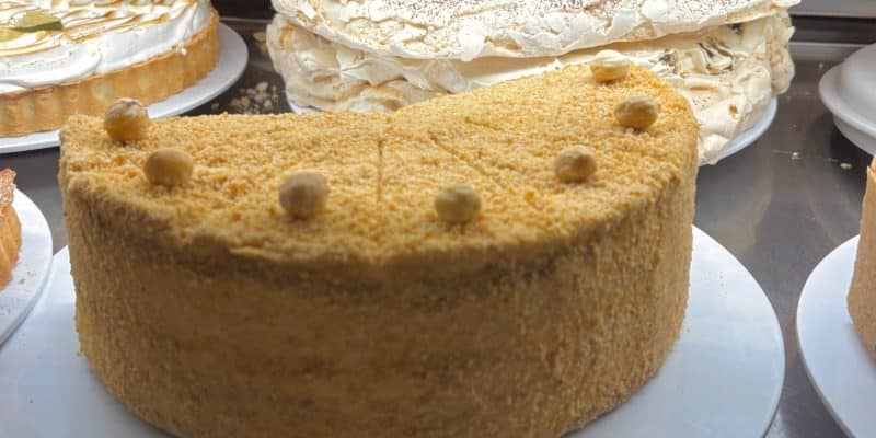 In der Kuchentheke des Lodz Bistro stehen verschiedene Torten, darunter eine mit Haselnüssen verzierte Honigtorte im Vordergrund sowie eine Baisertorte mit Kakaopulver und ein Zitronenbaiser-Tartelette im Hintergrund.