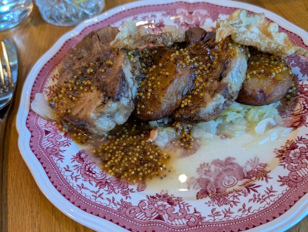 Ein Gericht im Lodz Browar Księży Mlyn mit gebratenem Fleisch, das mit einer grobkörnigen Senfsauce überzogen ist und auf einem Bett aus Sauerkraut sowie knuspriger Schweineschwarte serviert wird.