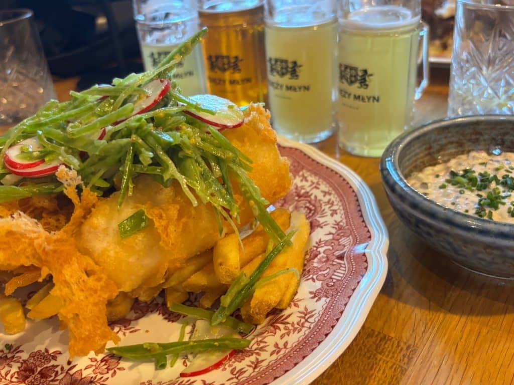 Ein Teller Fish and Chips mit Erbsenschoten-Salat und Radieschen, serviert mit einer Schale Remoulade und mehreren Gläsern Bier in der Brauerei Browar Księży Młyn in Łódź.