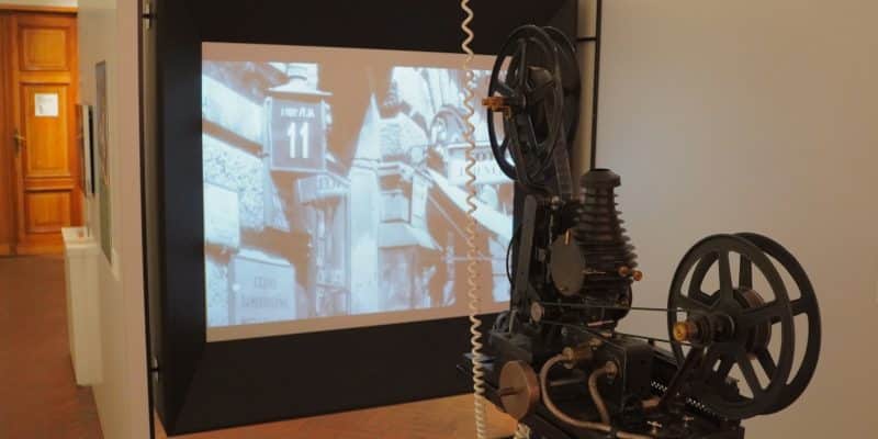 Ein historischer Filmprojektor im Filmmuseum Łódź projiziert einen Schwarz-Weiß-Film auf eine Leinwand, die eine Straßenszene mit der Hausnummer 11 zeigt.