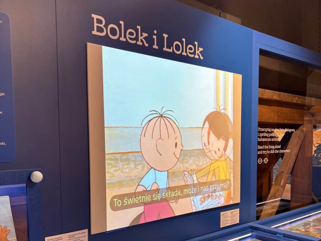 Eine Ausstellungsfläche im Filmmuseum Łódź zeigt eine Szene aus der Zeichentrickserie „Bolek und Lolek“ auf einem großen Bildschirm unter dem entsprechenden Schriftzug. Die beiden Jungen sind in einer Animation zu sehen, wobei am unteren Bildrand ein polnischer Untertitel eingeblendet ist.