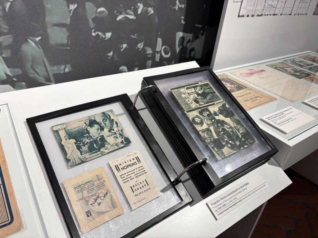 Eine Nahaufnahme zeigt historische Kinoprogrammhefte aus dem Filmmuseum in Łódź, die in einem aufgeschlagenen, schwarzen Ringbuch in einer Museumsvitrine präsentiert werden. Die Hefte aus den Jahren 1935–1938 enthalten Schwarz-Weiß-Fotografien von Filmszenen und Ankündigungen für Filme wie „Becky Sharp“ mit Miriam Hopkins.