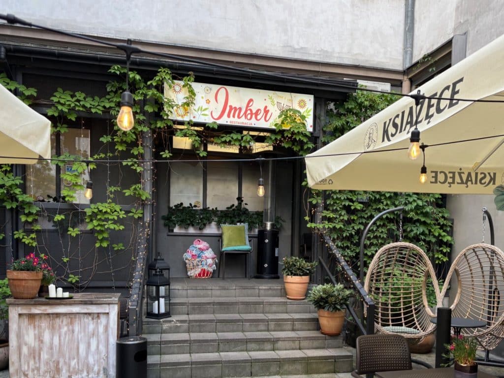Der gemütliche Außenbereich des Restaurants Imber in Łódź mit einer bepflanzten Treppe, hängenden Glühbirnen und stilvollen Korbsesseln unter einem Sonnenschirm.