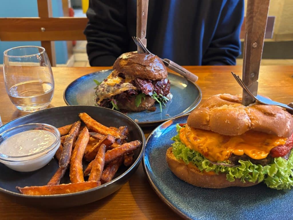 Zwei Burger mit geschmolzenem Käse und eine Schale Süßkartoffelpommes mit Dip stehen auf einem Holztisch im Restaurant Imber in Łódź.