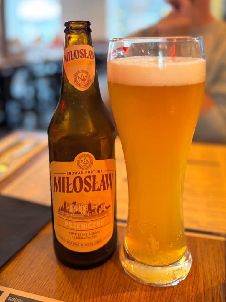 Eine Flasche und ein volles Glas Miłosław Pszeniczne Bier auf einem Holztisch im Restaurant Spółdzielnia in Łódź.