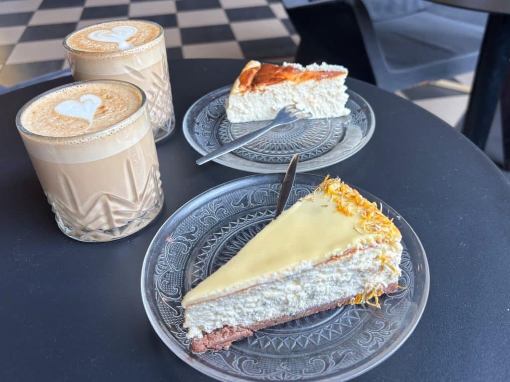 Zwei Gläser mit Latte Art und zwei Stücke Käsekuchen, serviert auf Glastellern im Szykier Coffee in Łódź.