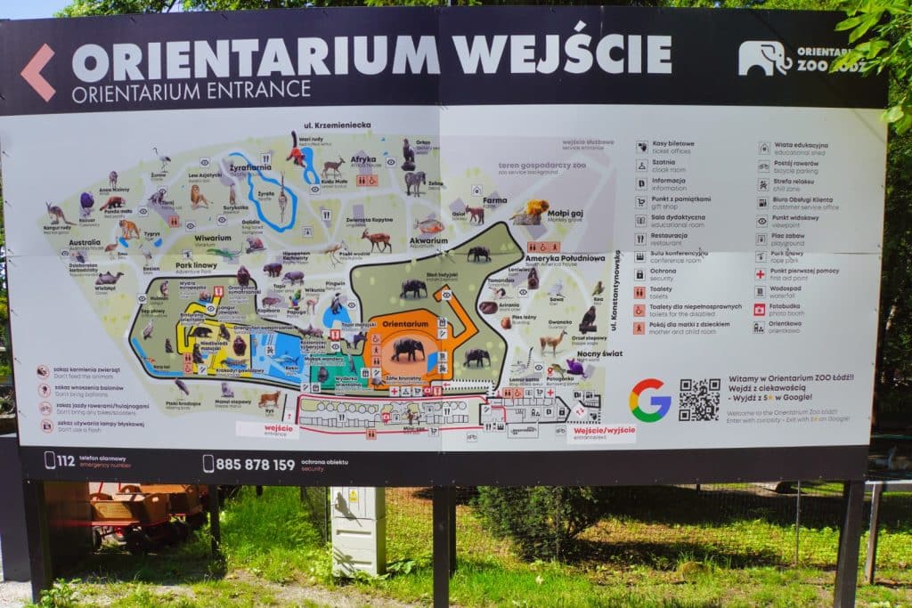 Ein großes Hinweisschild zeigt den detaillierten Orientierungsplan des Orientarium Zoo Lodz mit verschiedenen Tiergehegen, Wegen und Serviceeinrichtungen sowie einer Legende in polnischer und englischer Sprache. Über der Karte steht in großen Buchstaben „ORIENTARIUM WEJŚCIE“ mit einem Pfeil, der nach links weist.