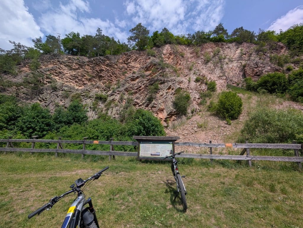 Zwei Mountainbikes stehen auf einer Wiese vor einem hölzernen Zaun und einer Informationstafel, im Hintergrund ragt eine steile, rötliche Felswand während einer Radtour in Niederschlesien empor.