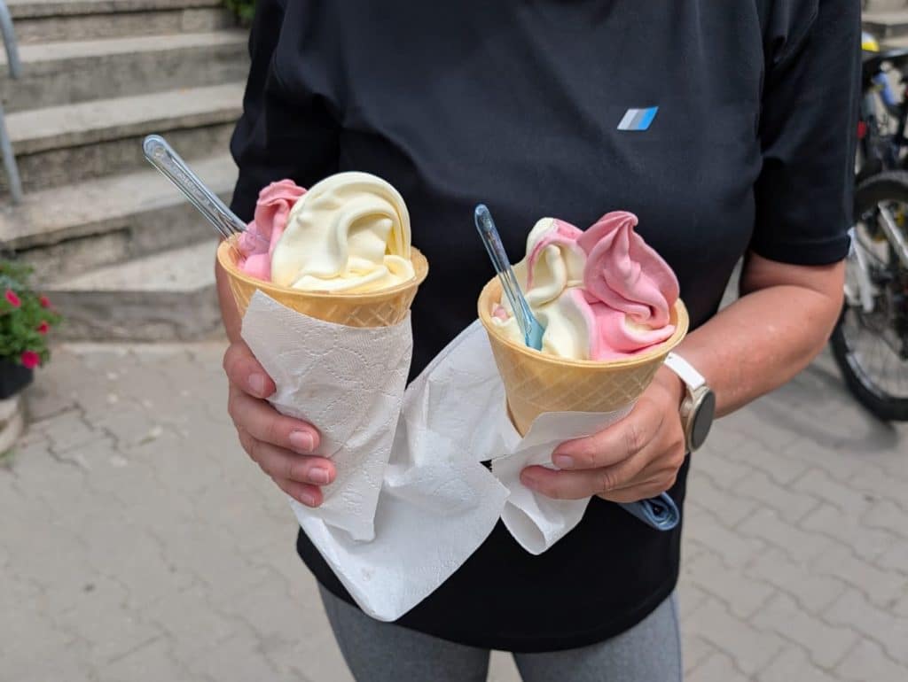 Eine Person hält zwei Waffelbecher mit rosa-weißem Softeis in den Händen, die während einer Radtour durch Niederschlesien genossen werden.