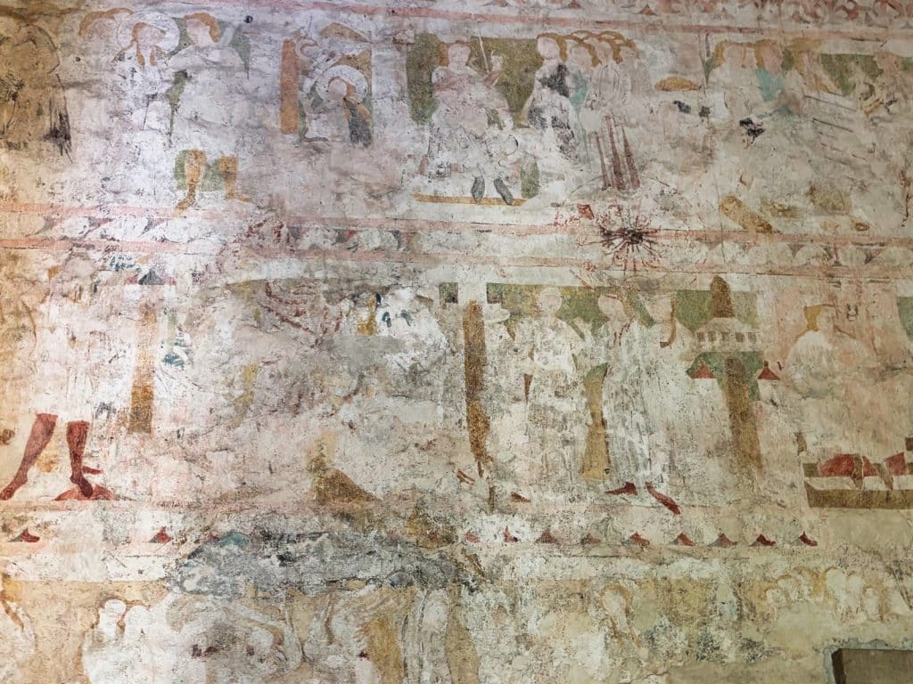Historische, mehrfarbige Wandbilder in einer niederschlesischen Kirche zeigen in mehreren horizontalen Registern verblasste biblische Szenen und menschliche Figuren.
