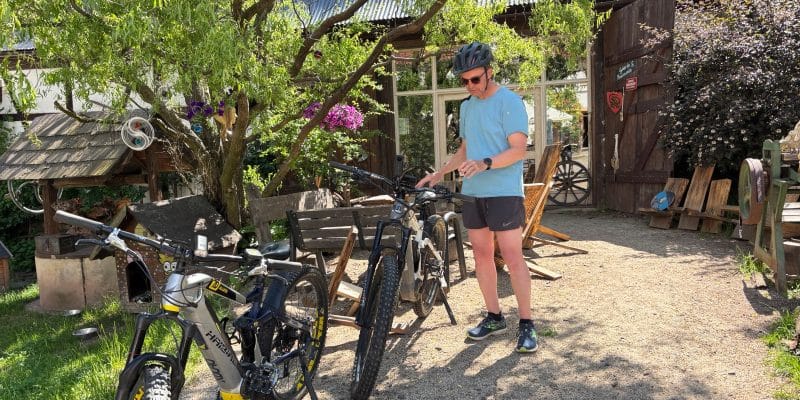 Ein Mann in Sportkleidung führt vor einer rustikalen Scheune in Niederschlesien einen Radcheck an seinem E-Mountainbike durch, während ein zweites Rad im Vordergrund bereitsteht.