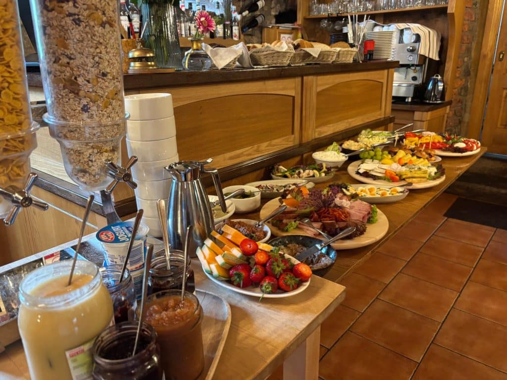Ein reichhaltiges Frühstücksbuffet in der Villa Greta in Niederschlesien mit Müsli-Spendern, frischem Obst, Aufschnittplatten, verschiedenen Aufstrichen und Brotbeilagen auf einer hölzernen Theke.