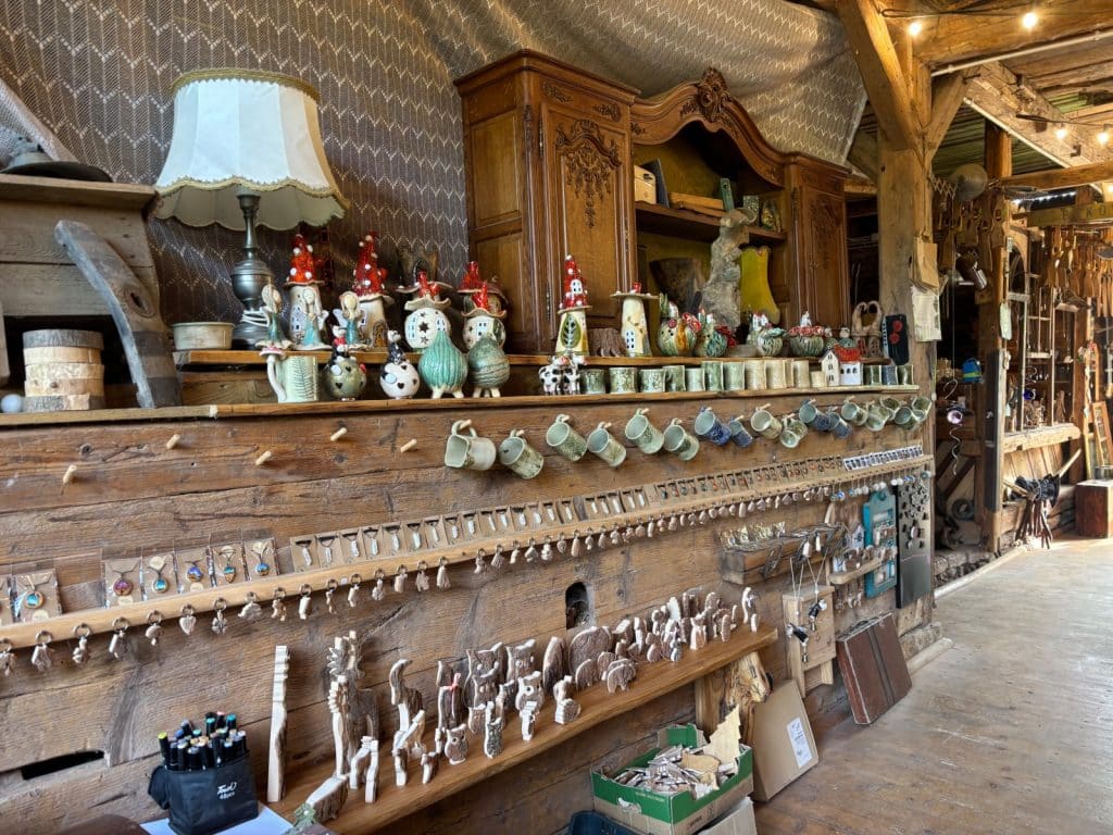 In der Galerie der Villa Greta in Niederschlesien werden zahlreiche kunsthandwerkliche Verkaufsartikel wie Keramikfiguren, Tassen, Schmuck und kleine Holzskulpturen auf rustikalen Holzregalen präsentiert.
